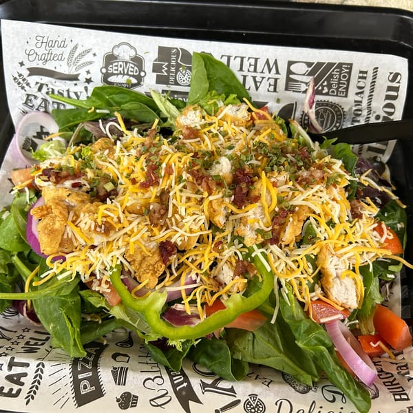 A vibrant salad with mixed greens, fried chicken, shredded cheese, bacon bits, and green onions.