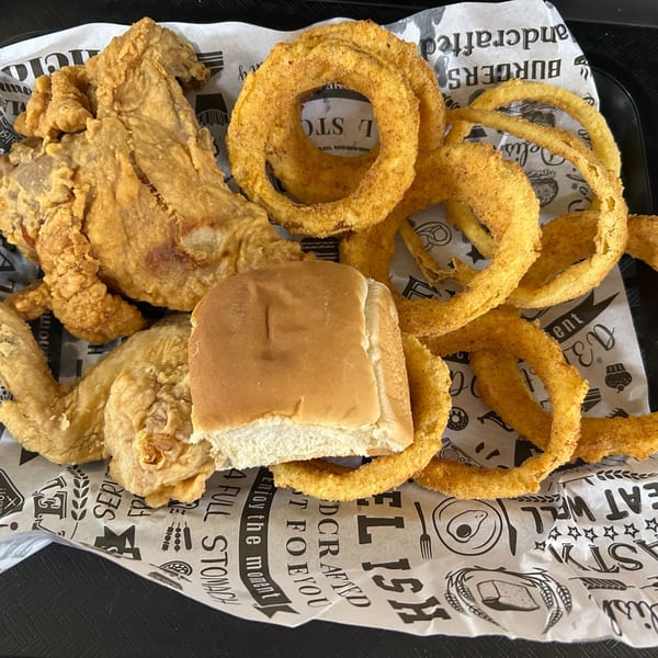 Crispy fried chicken pieces, golden onion rings, and a dinner roll on branded paper.