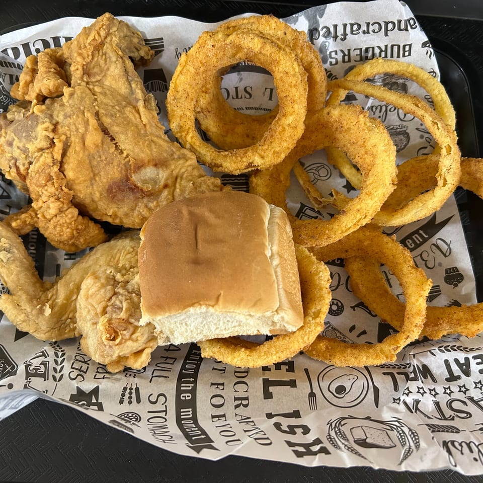 Crispy fried chicken pieces, golden onion rings, and a dinner roll on branded paper.