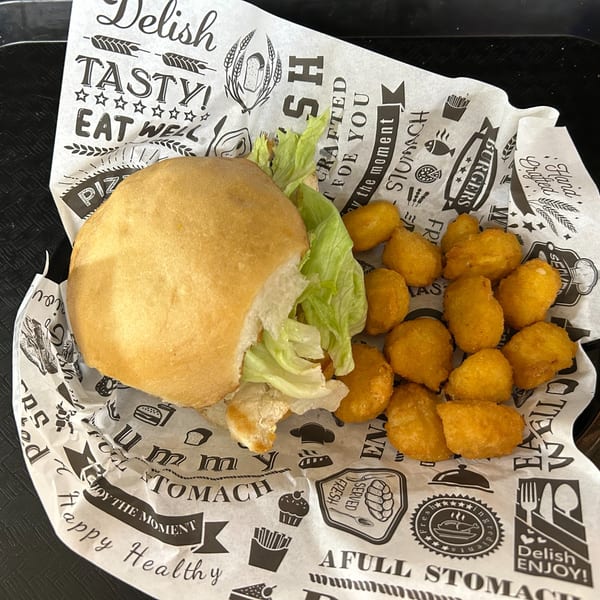 A burger with lettuce and a side of golden-brown chicken nuggets on patterned paper.